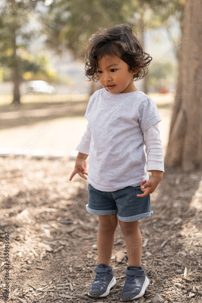 childhood lifestyle of a little girl with curly hair standing in a park, wear a shorts and blouse for summer, sunny day childhood lifestyle of a little girl with curly hair standing in a park, wear a shorts and blouse for summer, sunny day