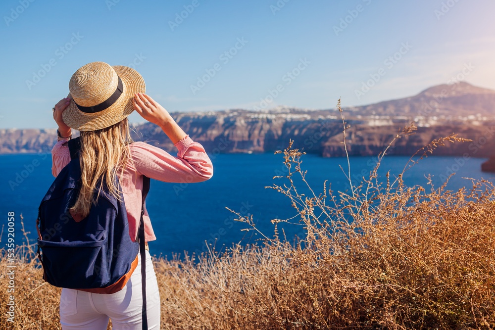 Traveler woman admires Santorini island, Greece enjoying sea landscape. Happy hiker with backpack looks at Caldera