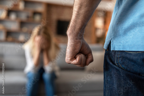 Frightened crying mature caucasian wife afraid of her husband, man threatening with fist photo