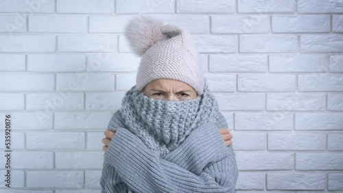 Lady with problem central heating. A young frustrated woman in woolen scarf freezing in a flat with cool temperature. A concept of heating crisis in the world.