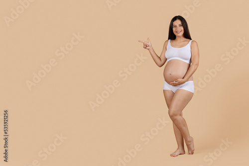 Pregnancy Ad. Beautiful Smiling Pregnant Woman In Underwear Pointing Aside At Copy Space © Prostock-studio