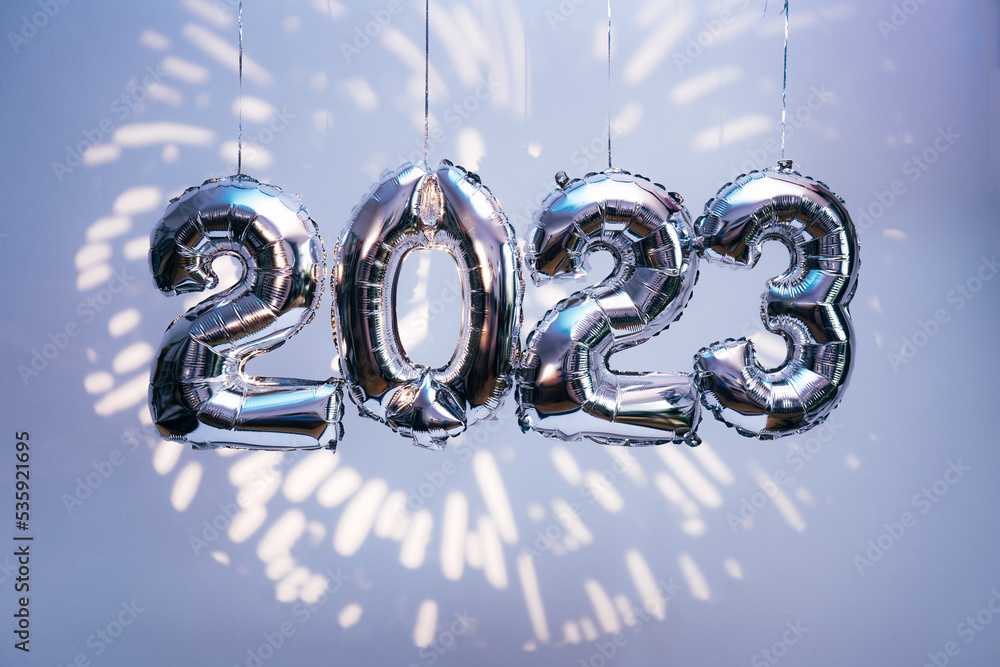 Silber foil balloons in numbers shape 2023 hanging against blue wall with fireworks projection. New Year holidays - obrazy, fototapety, plakaty 