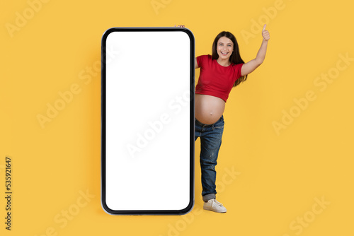 Nice Promo. Positive Pregnant Woman Peeking Out Behind Big Blank Smartphone