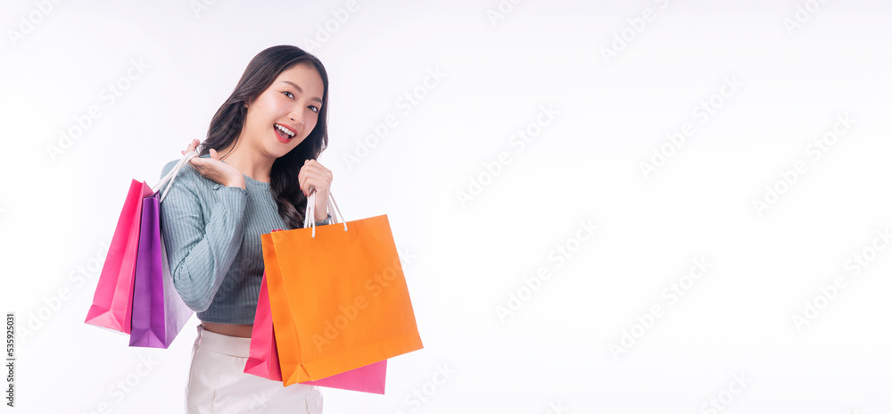 Enjoyment excited asian woman carry shopping bags standing on white background. Trendy happy shopper consumer carefree young girl holding shopping paper bags with copy space over isolated background. Enjoyment excited asian woman carry shopping bags standing on white background. Trendy happy shopper consumer carefree young girl holding shopping paper bags with copy space over isolated background.