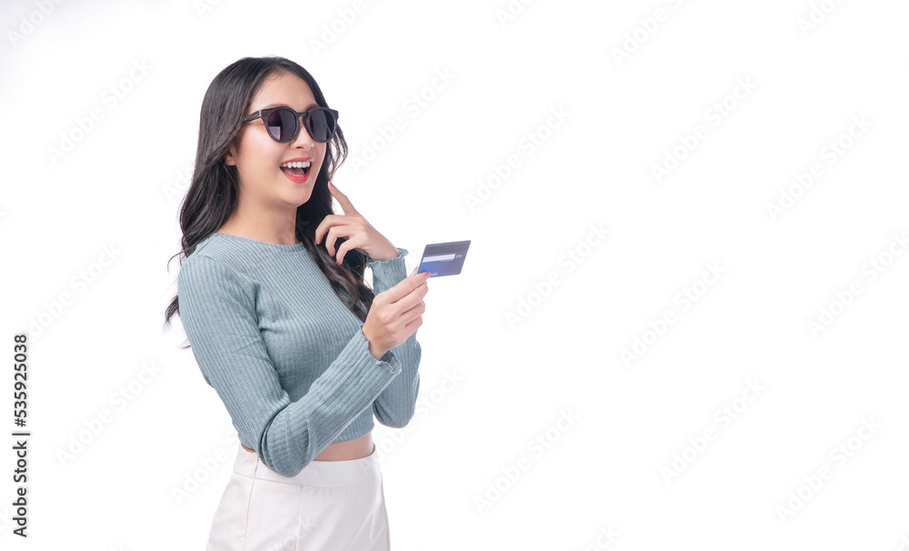 Excited asian woman wear sunglasses showing credit card in hand standing on white background. Cheerful surprised young girl holding blank card for payment online over isolated. Finance shopping online Excited asian woman wear sunglasses showing credit card in hand standing on white background. Cheerful surprised young girl holding blank card for payment online over isolated. Finance shopping online