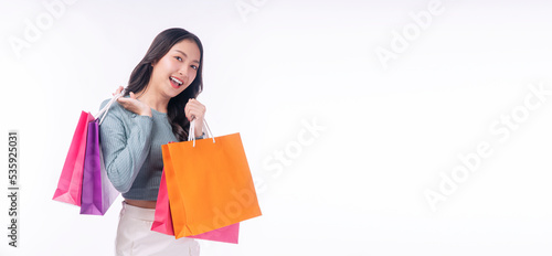 Enjoyment excited asian woman carry shopping bags standing on white background. Trendy happy shopper consumer carefree young girl holding shopping paper bags with copy space over isolated background.