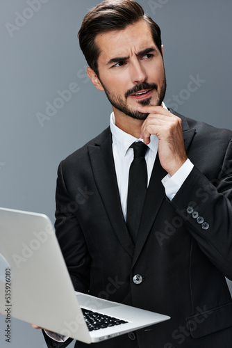 Man business looks into laptop and works thoughtfully online via internet in business suit video call business talks on gray background copy place