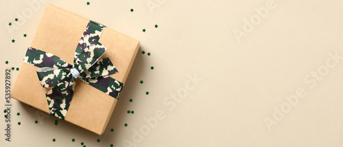 Fotografie Gift box with camouflage military ribbon bow and confetti on beige background