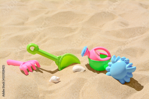 Bright plastic rake and shovel on sand. Beach toys. Space for text