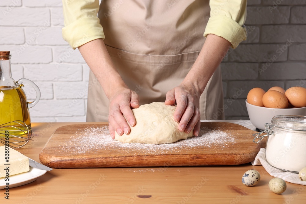 Woman kneading dough at wooden table near white brick wall, closeup Woman kneading dough at wooden table near white brick wall, closeup