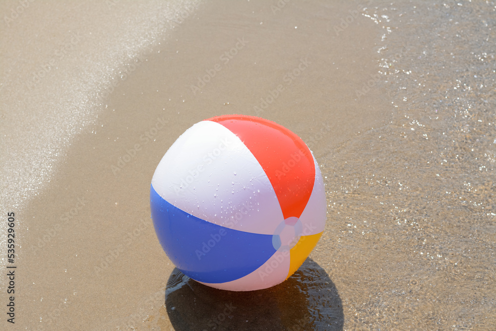 Colorful beach ball on wet sand at seaside