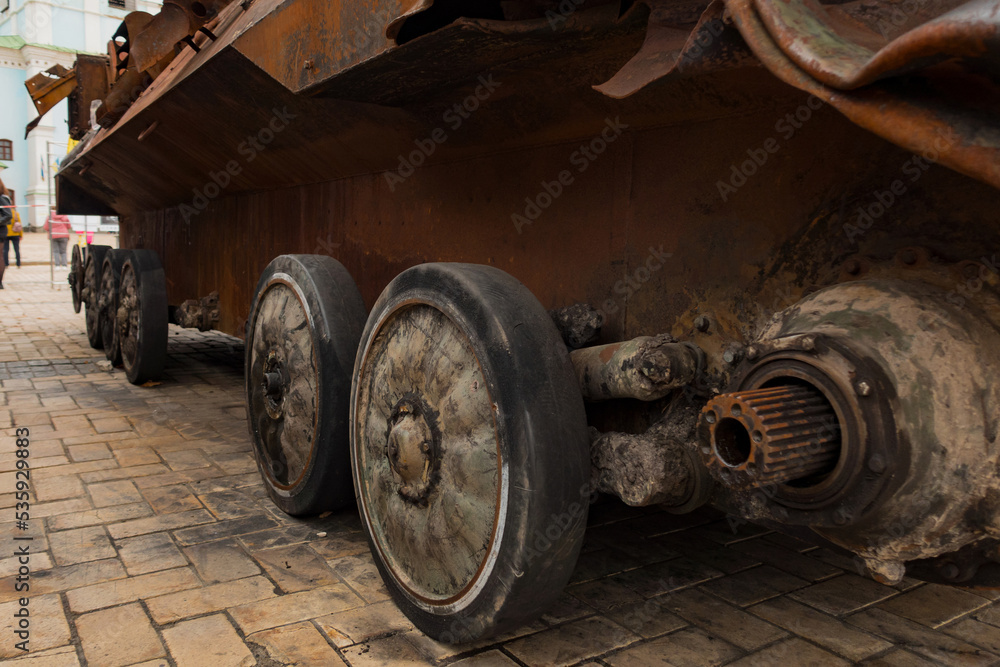 The destroyed wheels of a rusty military vehicle stand outdoors on the street. Attack. Conflict. Destruction. Tank. Broken. Equipment. Rusty. Russia. Russian. Battle. Damage. Fight. Heavy. Defense