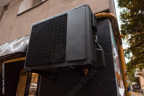 Black air-conditioner hanging on the facade of the building. Structure. Exterior. Town. Climate. Cool. Fan. Heat. System. Conditioner. HVAC. Temperature. Air. Cooler. Technology