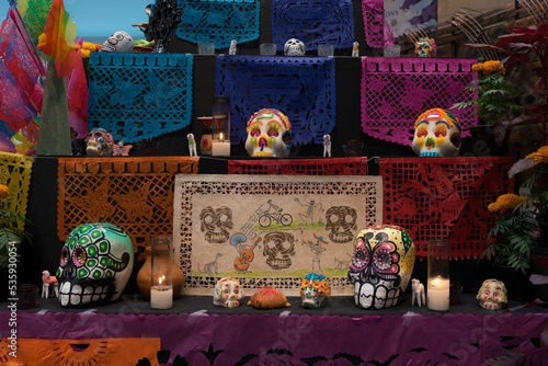 Colorful and painted day of the dead skulls, calaveras on an altar with papel picado, lighted candles and flowers