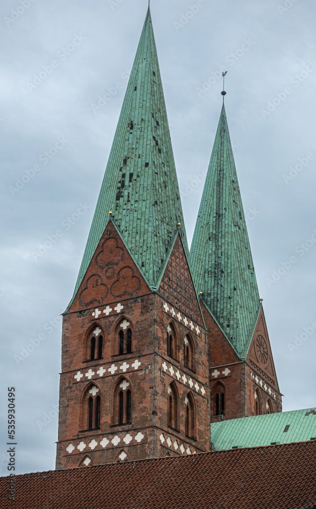 Germany, Lubeck - July 13, 2022: Closeup of 2 Marienkirche, Mary's church, green steeples against light blue sky, on top of red-brown brick towers