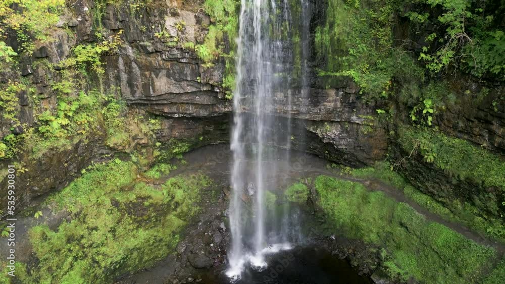 Upward panning camera view of a large waterfall in a lush, green forest Upward panning camera view of a large waterfall in a lush, green forest