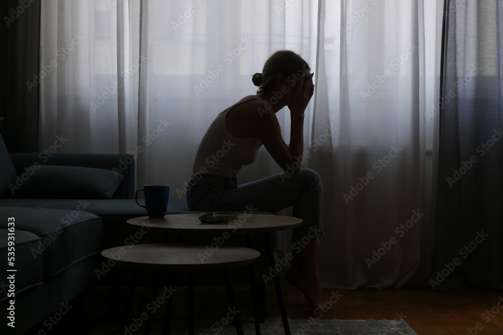 Young depressed woman sitting on the sofa next to the window