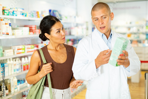 Male pharmacist consulting oriental woman about treatment in drugstore.