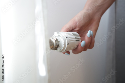Woman's hand adjusting radiator thermostat valve, controlling central heating system photo