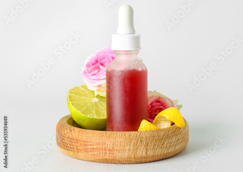 Wooden bowl with bottle of citrus serum on grey background