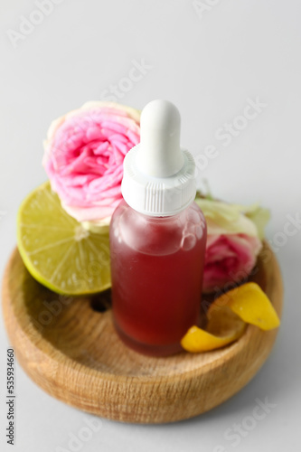 Wooden bowl with bottle of citrus serum on grey background, closeup