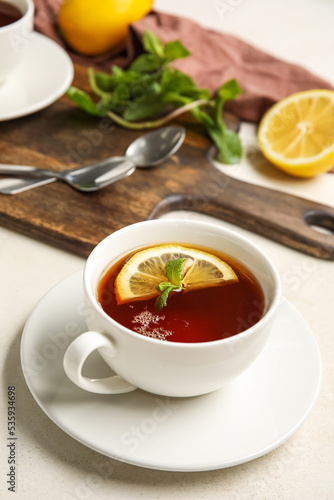 Cup of black tea with lemon and mint on white table, closeup