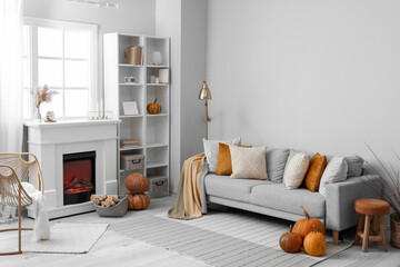 Autumn interior of living room with grey sofa, fireplace and pumpkins
