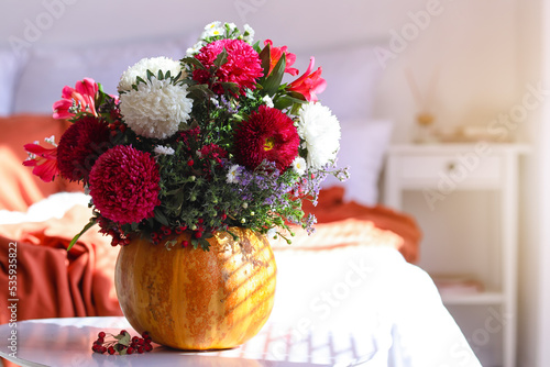 Pumpkin with autumn flowers on table in light bedroom, closeup