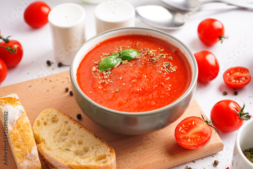 Wooden board with bowl of tasty tomato soup and bread on light background, closeup
