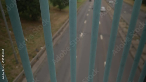 Looking through bars on bridge with Cars passing underneath photo