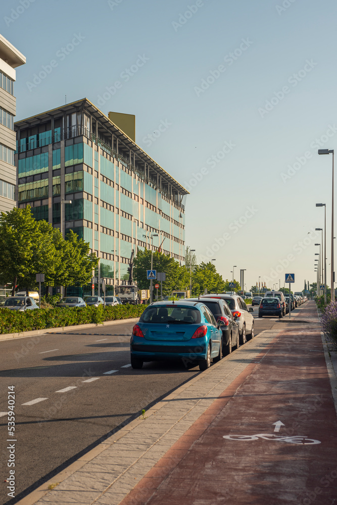 A city street with a bike lane, parked cars, tree lined median and office buildings