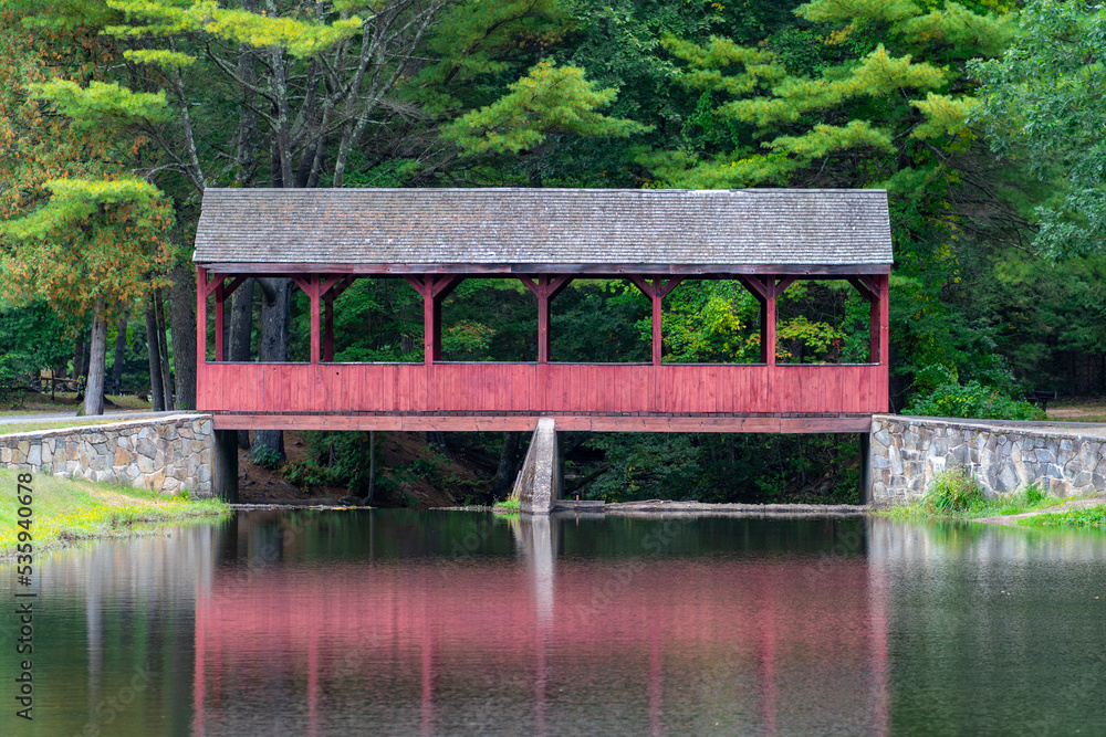 Red covered bridge rests over a fishing pond in early Autumn 2022.
