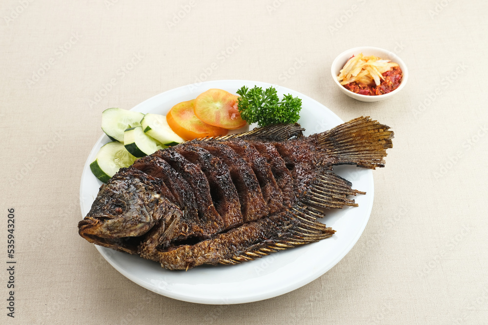 Gurame Bakar Madu, Grilled Gourami with honey and soy sauce. Served with sambal (chilli sauce), cucumber and tomatoes in white plate.
Gurame Bakar Madu, Grilled Gourami with honey and soy sauce. Served with sambal (chilli sauce), cucumber and tomatoes in white plate.