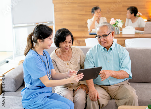 Beautiful Asian nurse or doctor use tablet to consult and give assistant to couple senior man and woman in living room of clinic or hospital in senior healthcare center.