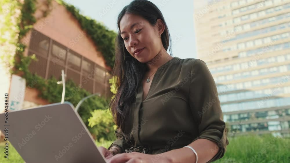 Young girl uses laptop pc outside on modern buildings background Young girl uses laptop pc outside on modern buildings background