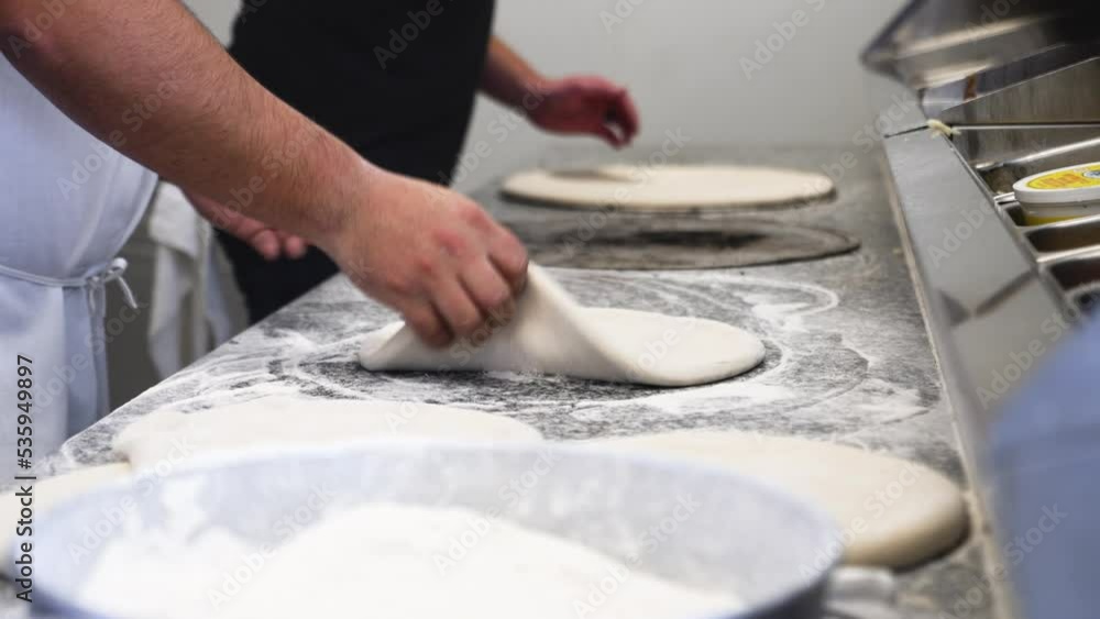 Pizza chef preps crust for toss, cook pulls and pats raw dough, chef ladles red sauce over prepped pizza dough, slow motion 4K Pizza chef preps crust for toss, cook pulls and pats raw dough, chef ladles red sauce over prepped pizza dough, slow motion 4K