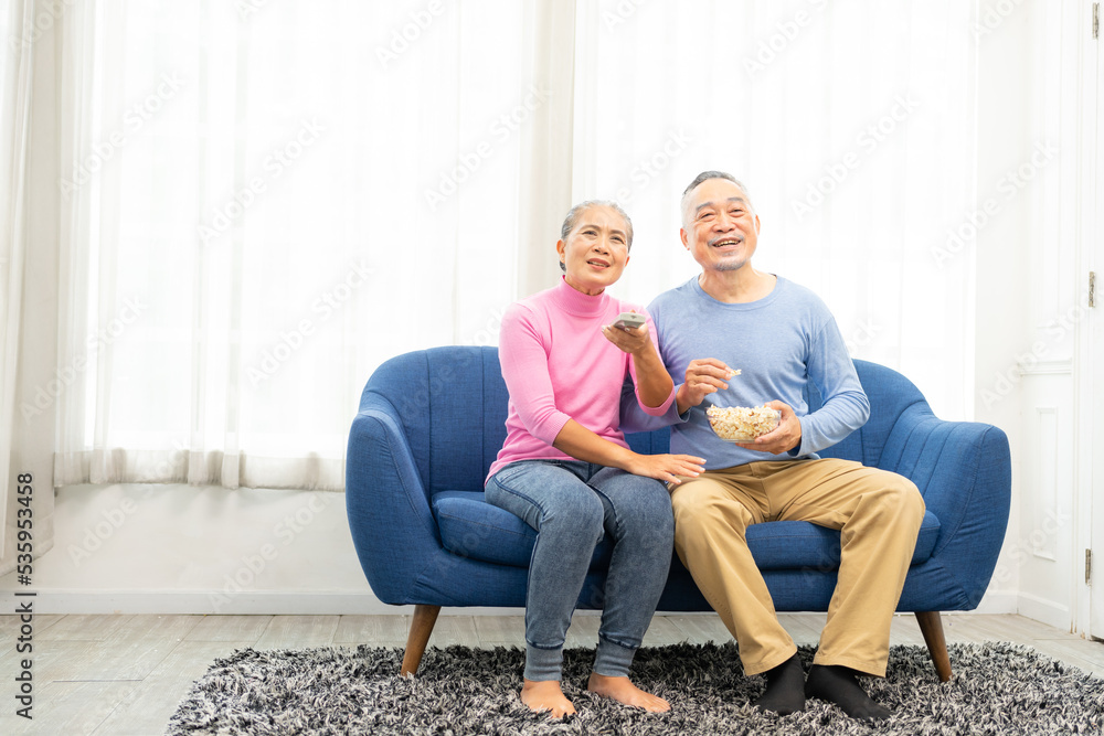 Happy smiling asian senior couple sitting on sofa and watching TV at home in living room. senior spending weekend time together.