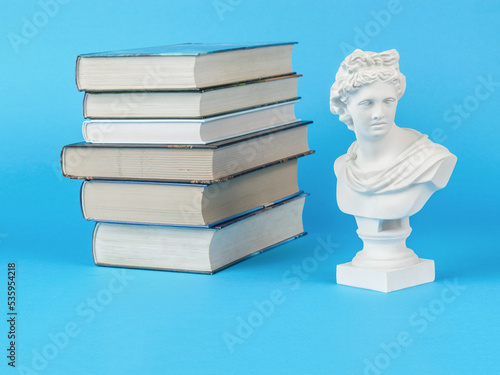 A stack of books and a plaster statuette on a light blue background. Minimal concept. photo