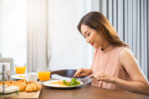 Asian young woman sitting kitchen table food having eating healthy breakfast at home, female eat fresh breakfast served food with beverage before go to work in the morning at home