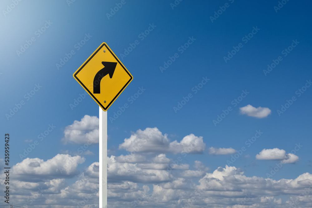 Traffic sign; right arrow curve sign on white pole by the main road with blue sky background, soft and selective focus. Traffic sign; right arrow curve sign on white pole by the main road with blue sky background, soft and selective focus.