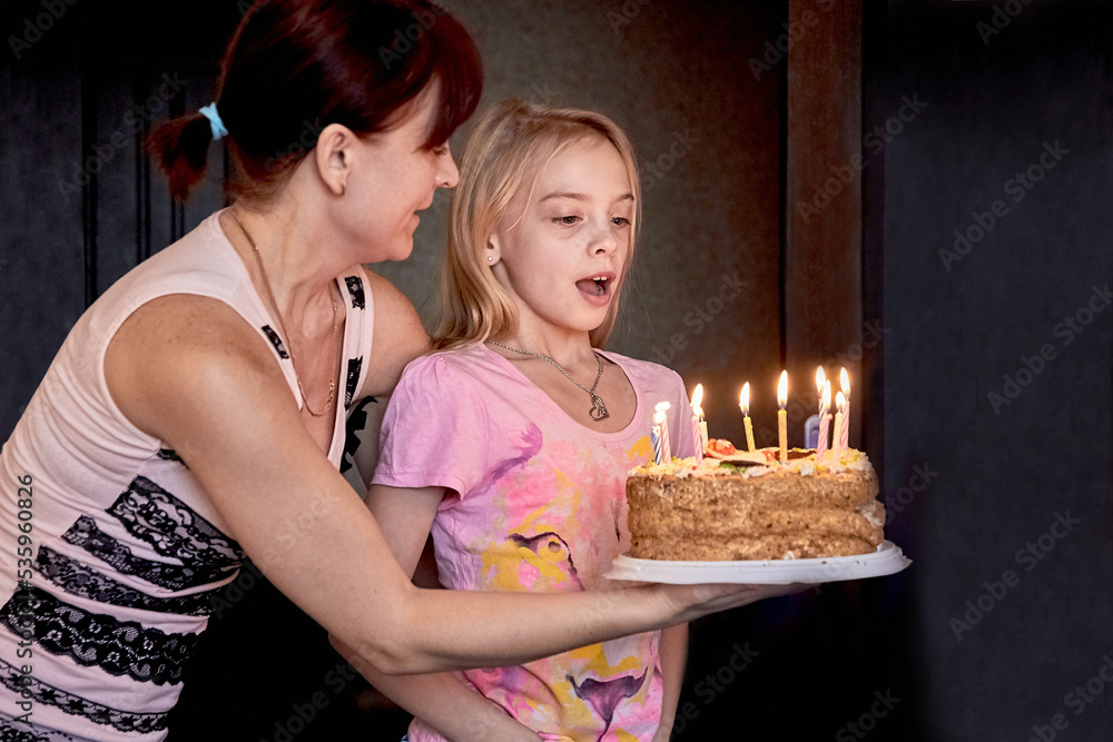 The happiest family.Mom with her cute daughter holds a cake for her daughter's birthday.A girl tries to blow out the candles on the cake