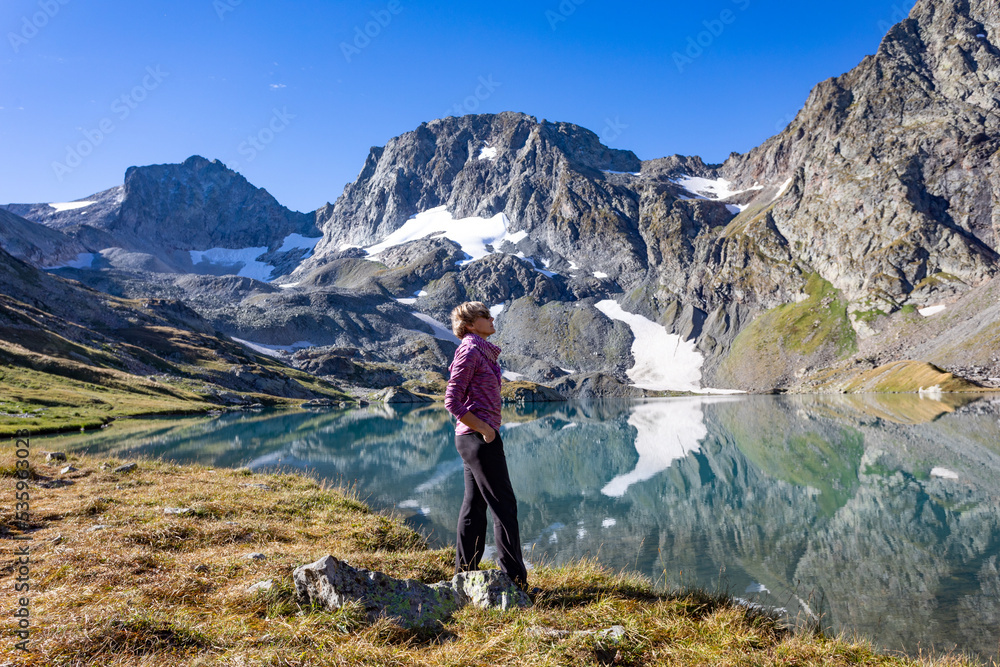 Naklejka premium The girl stands against the backdrop of mountain peaks and a blue lake. Beautiful mountain landscape for vacation, travel and healthy lifestyle