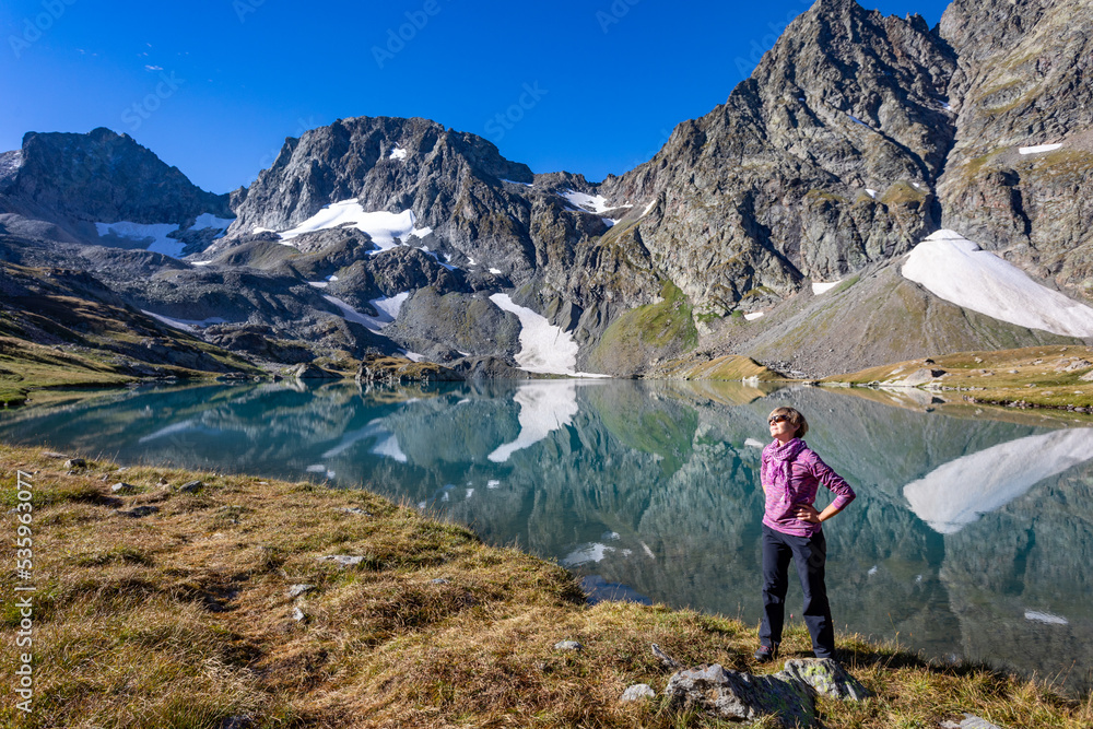 The girl stands against the backdrop of mountain peaks and a blue lake. Beautiful mountain landscape for vacation, travel and healthy lifestyle