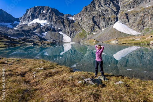 The girl stands against the backdrop of mountain peaks and a blue lake. Beautiful mountain landscape for vacation, travel and healthy lifestyle