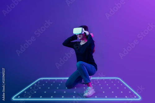 Asian woman wearing VR headset with new experience  playing video game and light mark zone area for play on futuristic purple cyberpunk neon light background. Metaverse technology concept. photo