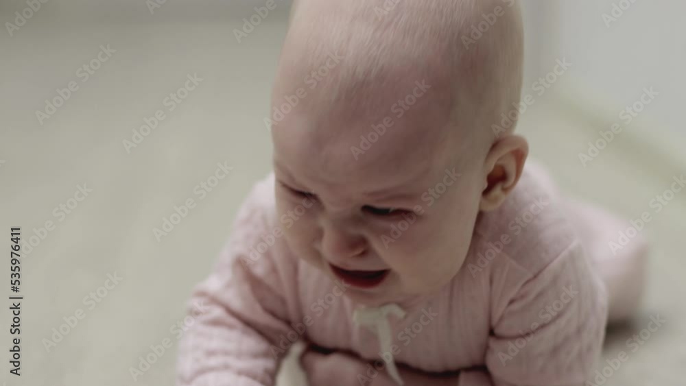Little caucasian girl aged 6 months is crying and crawling on the floor. Emotions on the face. Close-up Little caucasian girl aged 6 months is crying and crawling on the floor. Emotions on the face. Close-up