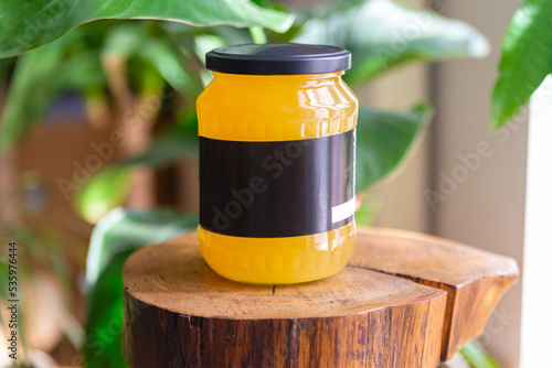 Obraz na płótnie A jar of honey on a wooden stem. Black label, flowers in the background. Illuminated jar by sunlight. w salonie