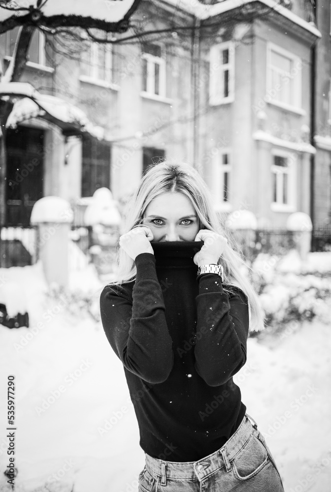 Black-white photo of a young girl in a black sweater and jeans posing on a background of winter street