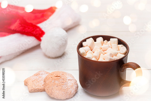 mug with marshmallows, santa hat and cookies on the table close-up