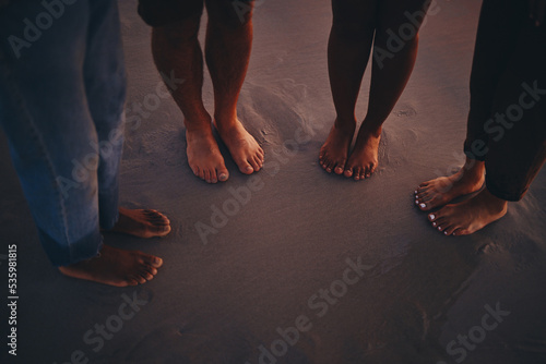 Friends, sand and feet at a beach at sunset, relax and bonding on summer vacation in nature. Toes, fun and people travelling and exploring at the sea, standing and enjoying holiday and friendship